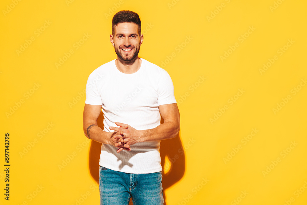 Portrait of handsome smiling stylish hipster lambersexual model. Sexy man dressed in white T-shirt and jeans. Fashion male isolated on yellow wall in studio Portrait of handsome smiling stylish hipster lambersexual model. Sexy man dressed in white T-shirt and jeans. Fashion male isolated on yellow wall in studio