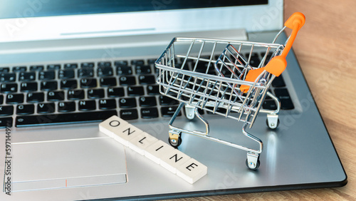 Online shopping concept. Black friday shopping online. Shopping cart or trolley and laptop on wooden table.