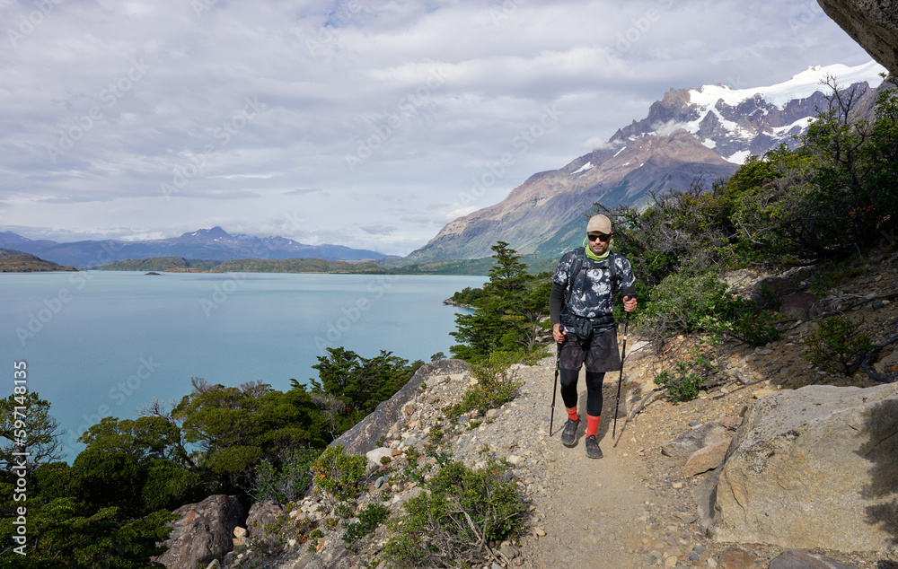 Mature hiker walking on a trail with a view of the lake and mountains in the background in Torres del Paine National Park