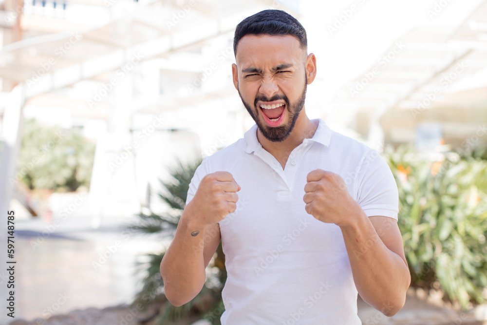 Fototapeta premium young handsome man shouting aggressively with annoyed, frustrated, angry look and tight fists, feeling furious