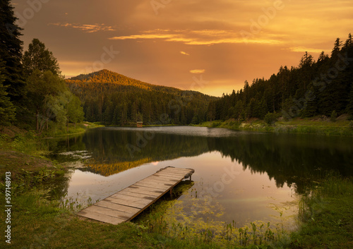 Fototapeta Naklejka Na Ścianę i Meble -  Small lake and pier at sunset.Mountain lake and pine forests.