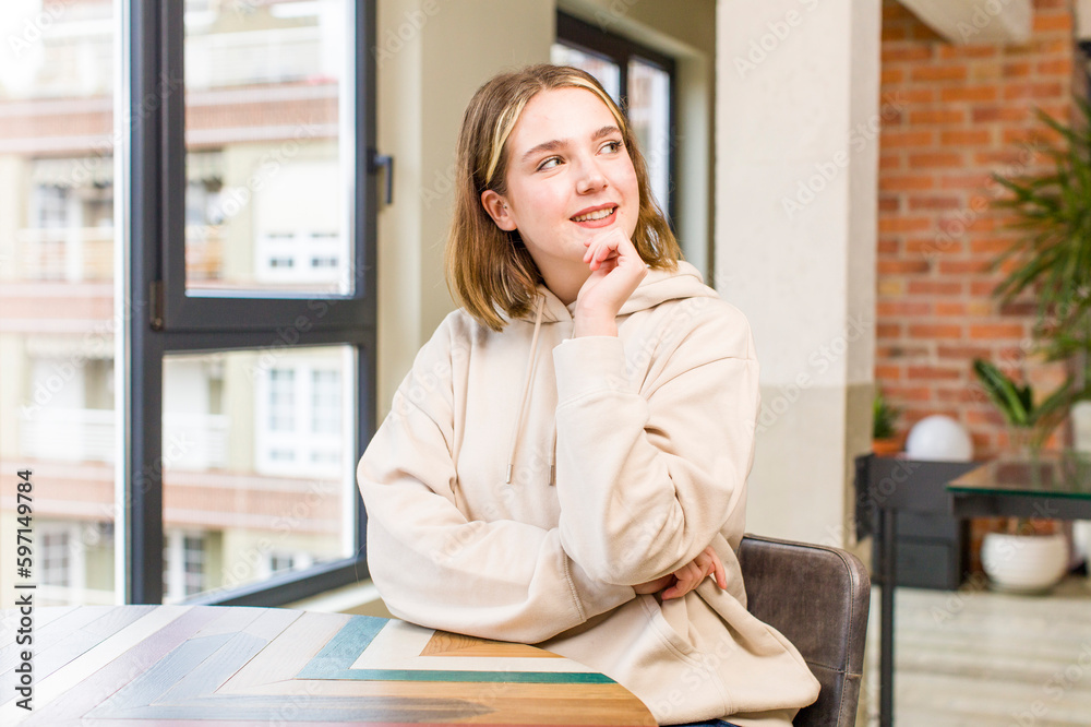 pretty caucasian woman smiling happily and daydreaming or doubting, looking to the side. home interior concept pretty caucasian woman smiling happily and daydreaming or doubting, looking to the side. home interior concept