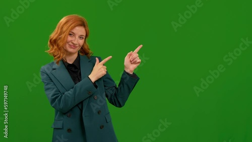 Woman looking into the camera, smiling showing to the left gestures with hands on green chroma key screen background. Female hand sign left, direction showing in front of chroma key. photo