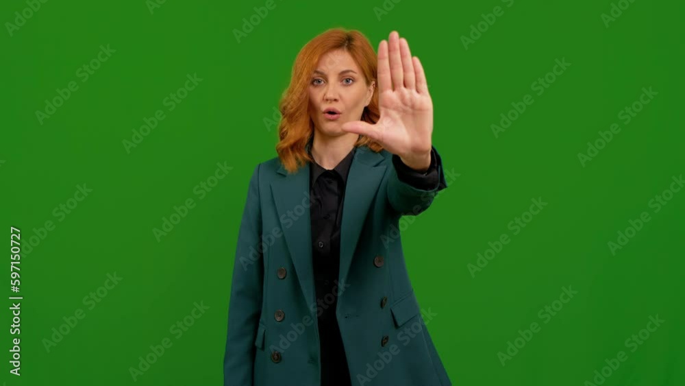 Pretty woman on green screen chroma key doing stop sign with left hand over isolated background. Female disaproval showed by hands to stop. Pretty woman on green screen chroma key doing stop sign with left hand over isolated background. Female disaproval showed by hands to stop.