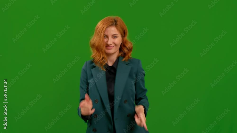 Female points at the camera and dances on green screen background. Happy lady in green jacket being excited.