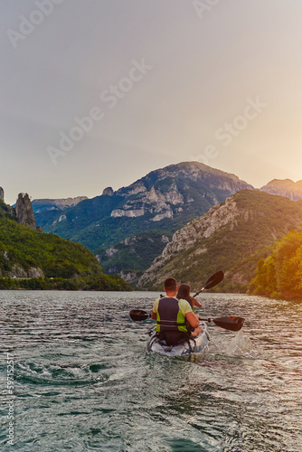 A young couple enjoying an idyllic kayak ride in the middle of a beautiful river surrounded by forest greenery in sunset time  © .shock