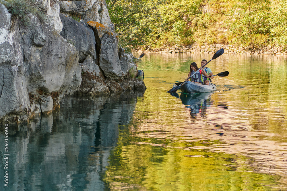 A young couple enjoying an idyllic kayak ride in the middle of a beautiful river surrounded by forest greenery A young couple enjoying an idyllic kayak ride in the middle of a beautiful river surrounded by forest greenery