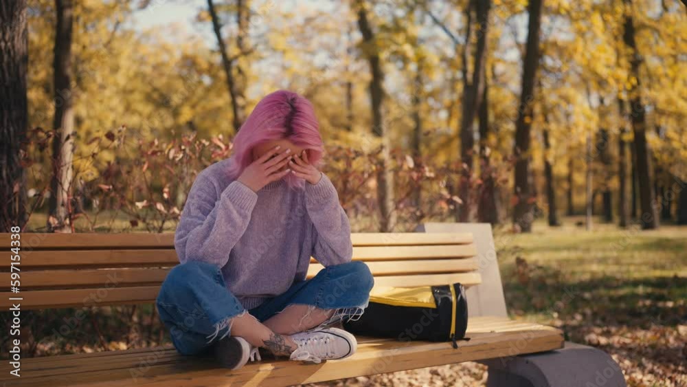 Young woman feeling upset while sitting on bench in park, relationship problems