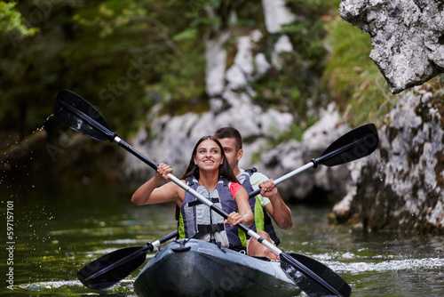 A young couple enjoying an idyllic kayak ride in the middle of a beautiful river surrounded by forest greenery