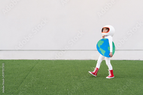 Girl wearing astronaut costume holding earth cut out walking on grass photo