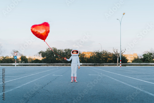 Girl wearing astronaut dress standing in parking lot holding heart shape balloon