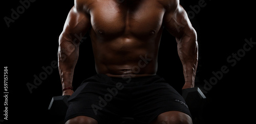 Muscular bodybuilder doing exercises with dumbbells on black background