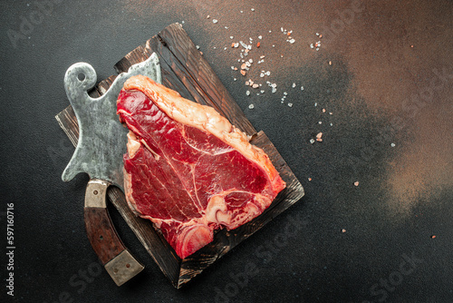 Meat Steaks T-bone between knife, on black stone background. Raw beef meat. place for text, top view