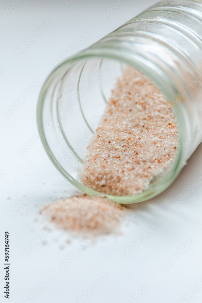 pink salt spill from small glass container on white background