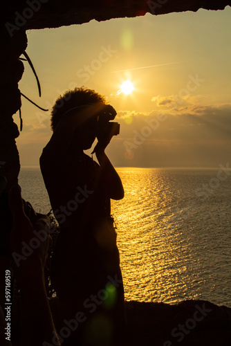 silhueta do perfil de uma fotógrafa fazendo uma foto de um lindo por do sol refletido no mar a sua luz dourada. photo