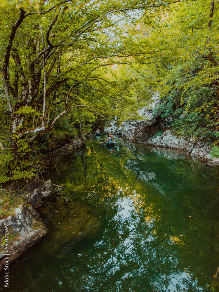 A group of friends enjoying having fun and kayaking while exploring the calm river, surrounding forest and large natural river canyons A group of friends enjoying having fun and kayaking while exploring the calm river, surrounding forest and large natural river canyons