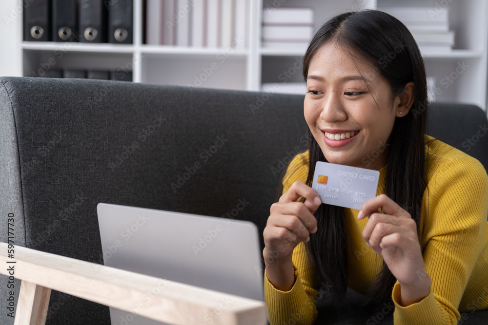 Pretty young woman shopping online with credit card and laptop while laying down on sofa at home. Pretty young woman shopping online with credit card and laptop while laying down on sofa at home.