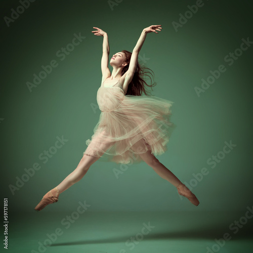 Foto Young and incredibly beautiful ballerina wearing tulle dress jumping gracefully over dark green studio background