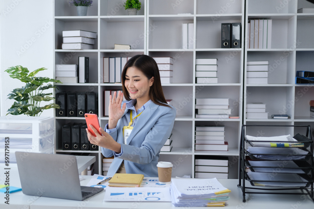 Beautiful Asian business woman having a video call with her friend, waving to a friend with smartphone. Beautiful Asian business woman having a video call with her friend, waving to a friend with smartphone.