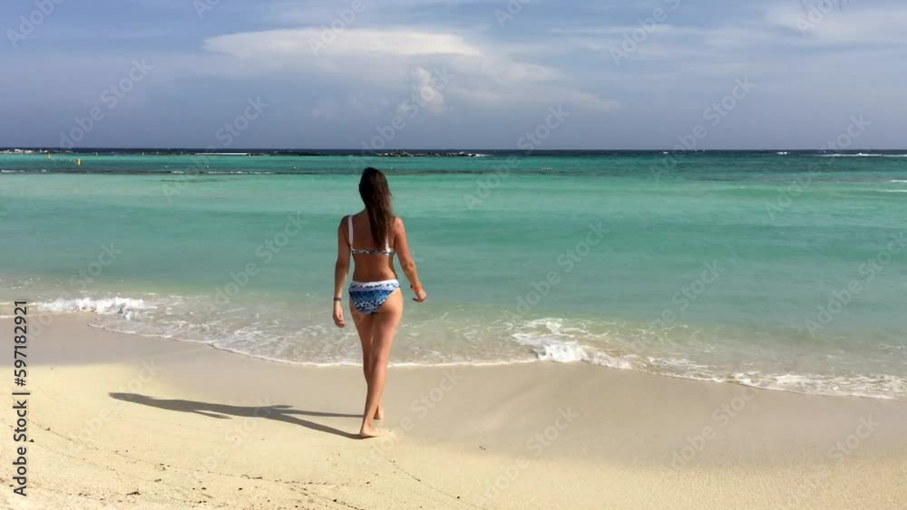 Young woman in blue bikini entering in beautiful blue water to swim on white sand beach in Aruba island in Caribbean Sea. High quality FullHD footage Young woman in blue bikini entering in beautiful blue water to swim on white sand beach in Aruba island in Caribbean Sea. High quality FullHD footage