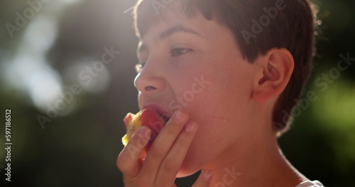 Young boy eating healthy fruit snack outdoors in the sunlight in picnic. Pensive child thinking while eating