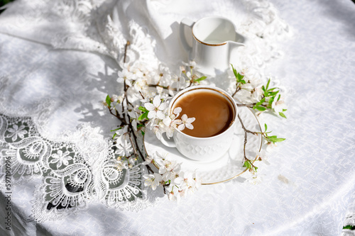 a cup of coffee on a table in a spring garden. Coffee with a milk jug and a branch of a flowering tree. Spring mood. Spring still life composition.