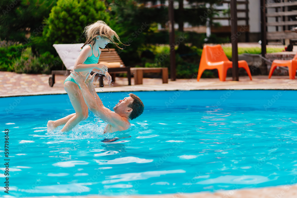 Dad and daughter play in the pool. dad throws daughter in the air.