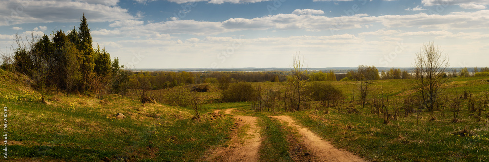 country dirt road through a hilly field. spring landscape. widescreen panoramic side view