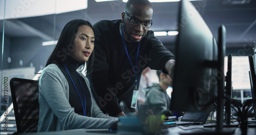 Two Diverse Multiethnic Colleagues Having a Conversation While Busy Working on a Team Project. Asian Female Designer Talking with an African Project Manager. Teamwork in Technology Laboratory