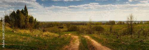 country dirt road through a hilly field. spring landscape. widescreen panoramic side view