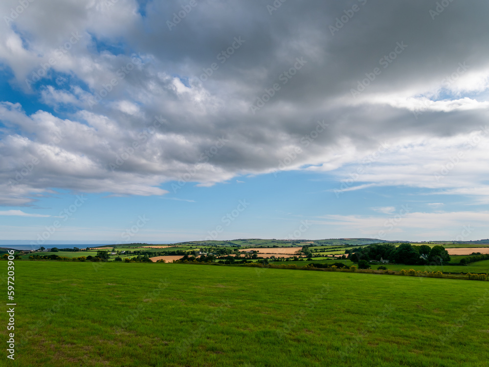 A cumulus cloud in the sky over the Irish countryside in summer. Irish landscape. Green farm fields. Green grass field under blue sky and white clouds