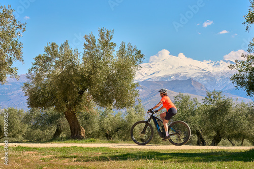 nice, active senior woman cycling with her electric mountain bike below the snow covered mountains of the Spanish Sierra Nevada, near Granada, Andalusia, Spain