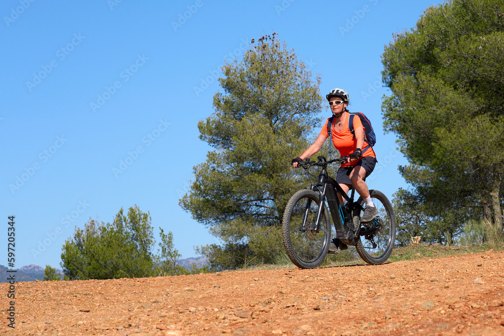 nice, active senior woman riding her electric mountain bike in the pine tree forests near Granada, Andalusia, Spain