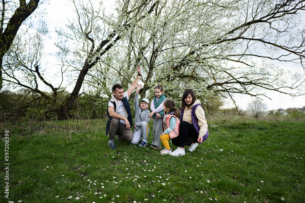 Family with three kids in spring meadow on the background of a flowering tree.