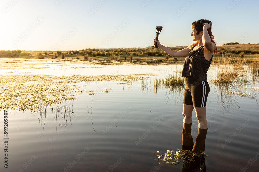 Woman taking selfie with camera in nature in middle of lake, surrounded ...