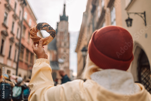 Tourist woman hand holding bagel obwarzanek, traditional polish snack in old city center view in Krakow, Europe. Back view photo