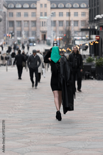 A woman with a perfect figure and red lips in a short black dress, a bright scarf on her head. Posing in the city