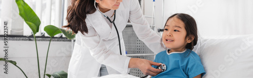 doctor with stethoscope examining cheerful asian girl in pediatric hospital  banner.