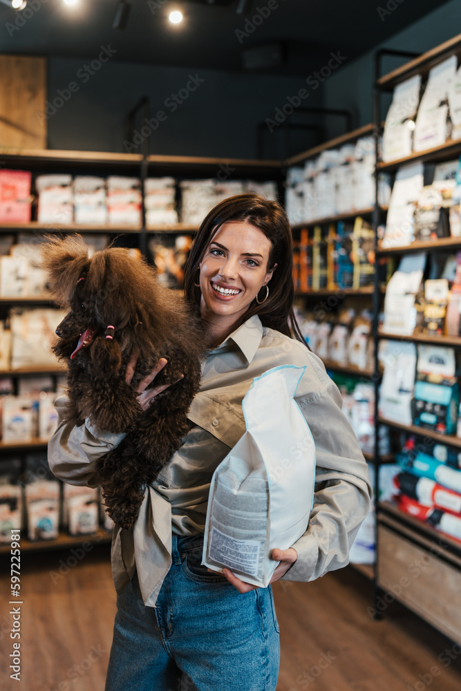 Beautiful young woman enjoying in modern pet shop together with her adorable brown toy poodle.