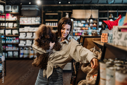 Beautiful young woman enjoying in modern pet shop together with her adorable brown toy poodle. photo