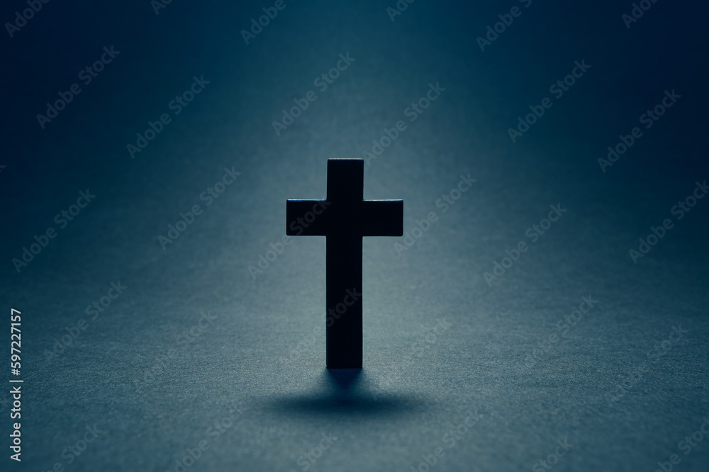Black religion catholic cross isolated on the dark solid fond blue background with the light coming from above