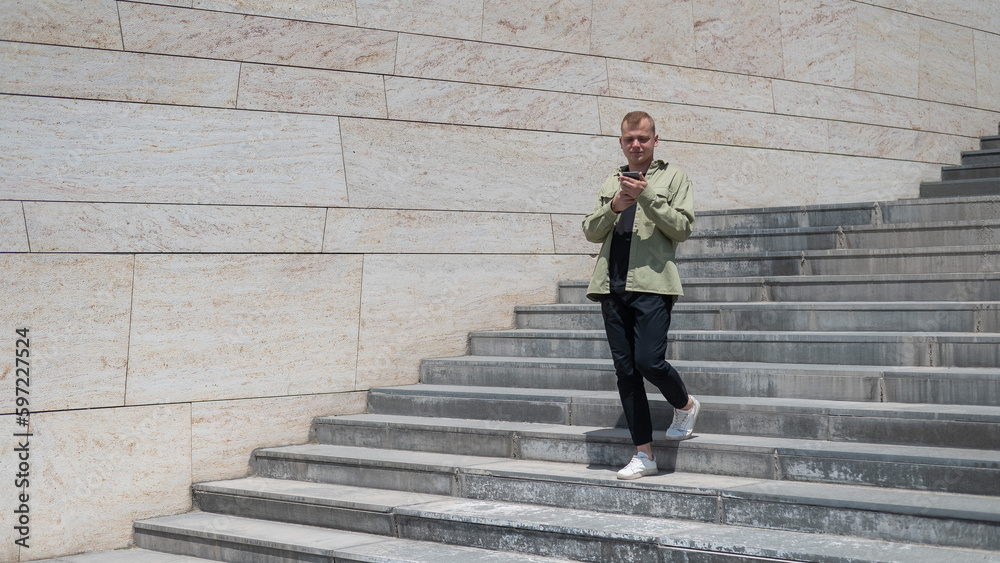 Young caucasian man using smartphone while going down stairs. 