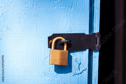 brass padlock securing a black metal hasp on a blue wooden door room for text photo