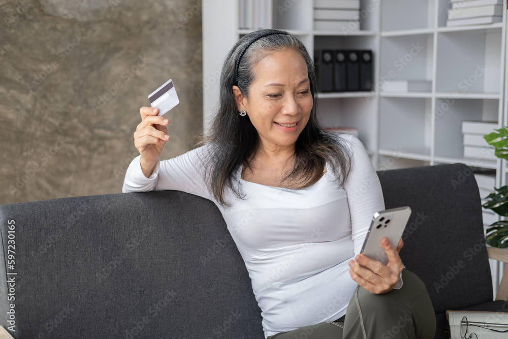 Relexed senior Asian woman is shopping online with her smartphone while sittng on the sofa. Relexed senior Asian woman is shopping online with her smartphone while sittng on the sofa.