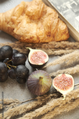 Gold autumn. Croissant, dark grapes, book and figs on the grey table