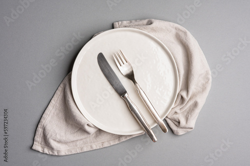 White flat empty plate with cutlery and napkin on a light gray background.