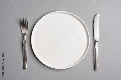 White flat empty plate with cutlery on a light gray background. Top view.