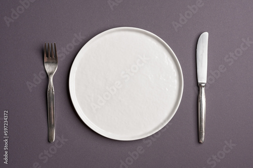 White flat empty plate with cutlery on a dark gray background. Top view.