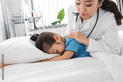 asian doctor calming depressed child obscuring face with pillow on hospital bed.