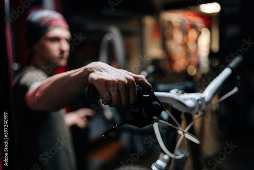 Close-up hands of unrecognizable mechanic insisting speed switches on mountain bike handlebar working in bicycle repair shop with dark interior. Concept of professional repair and maintenance of bike.